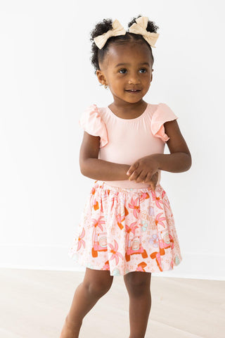 Young girl wearing a pink leotard and patterned skirt on a white background