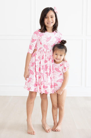 Two young girls wearing pink ballerina outfits standing on a white background