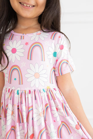 Child wearing a pink dress with rainbow and flower patterns on a white background