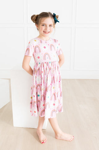 Young girl wearing a pink dress with rainbow pattern on a white background