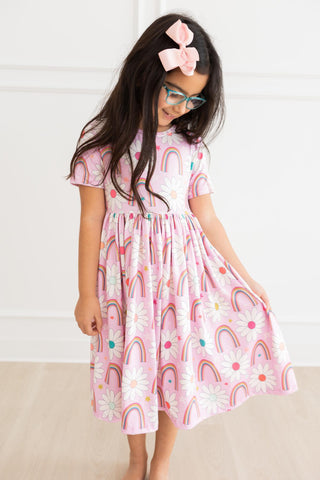 Young girl wearing a pink dress with rainbow pattern indoors.