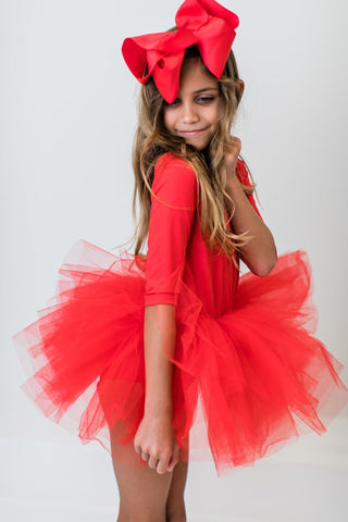 Young girl wearing a red tutu leotard with a large bow on a white background