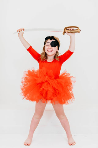Child in a red leotard with a tutu and eyepatch, holding a sword against a white background