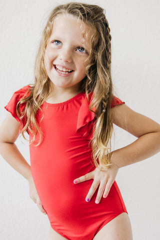 Young girl wearing a red leotard against a plain background