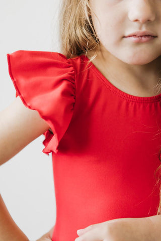 Close-up of a child wearing a red leotard with ruffled sleeves against a light background