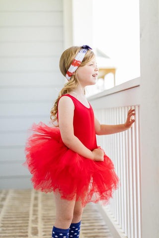 Young girl in a red leotard with a tutu standing on a staircase.