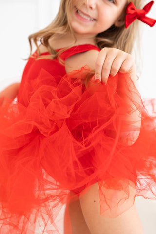 Child wearing a red leotard with a bow on a white background