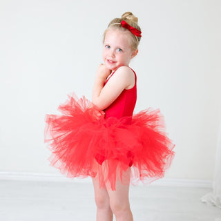 Young girl wearing a red tutu leotard against a white background