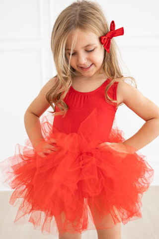 Young girl wearing a red tutu leotard with a bow in her hair on a white background