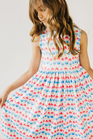 Young girl wearing a sleeveless dress with a colorful pattern on a plain background