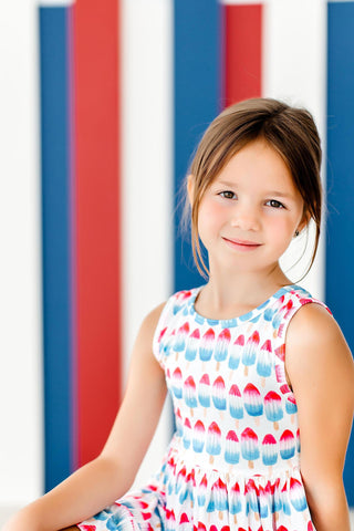 Young girl in a colorful dress sitting against a striped background