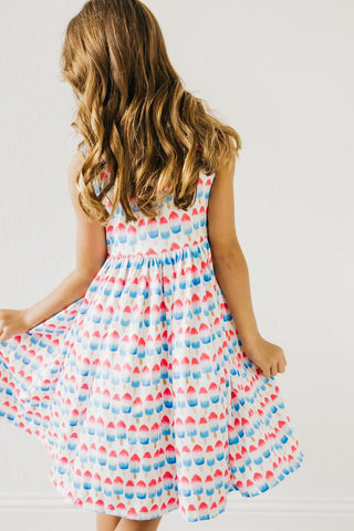 Young girl wearing a sleeveless dress with a colorful pattern on a plain background