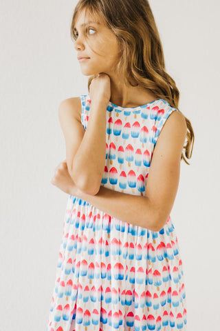 Young girl wearing a sleeveless dress with a colorful pattern on a plain background