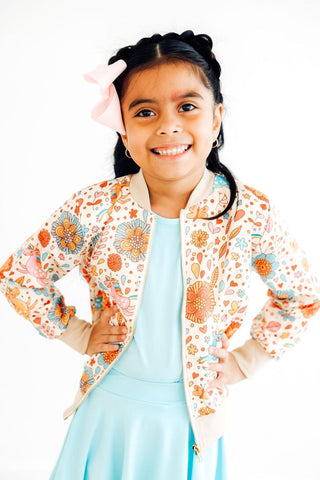 Young girl wearing a colorful floral jacket over a light blue dress on a white background