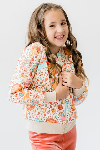 Young girl wearing a colorful floral jacket and pink pants on a white background