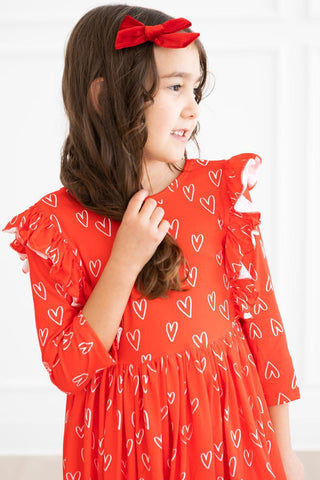 Young girl wearing a red dress with heart patterns and a red bow in her hair.