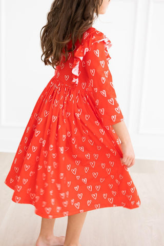 Red dress with white heart patterns worn by a child on a white background