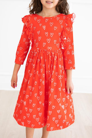 Child wearing a red dress with white heart patterns on a plain background