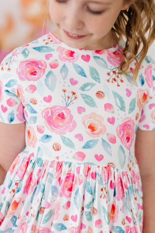 Child wearing a floral dress with pink flowers and leaves on a white background
