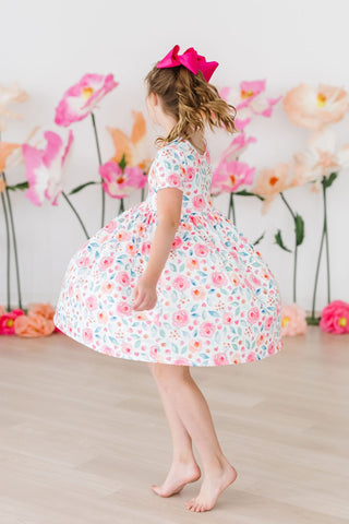 Young girl in a floral dress standing in front of pink flowers