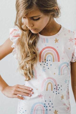 Young girl wearing a white t-shirt with colorful rainbow and star patterns.
