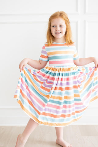Young girl wearing a colorful striped dress in a bright room.