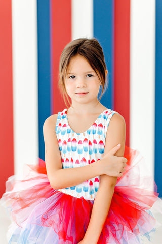 Young girl in a colorful leotard standing against a red, white, and blue striped background