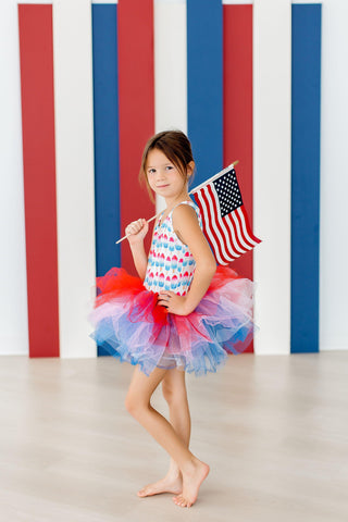 Young girl in a colorful tutu holding an American flag against a striped background