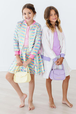 Two young girls in colorful outfits holding matching handbags on a white background