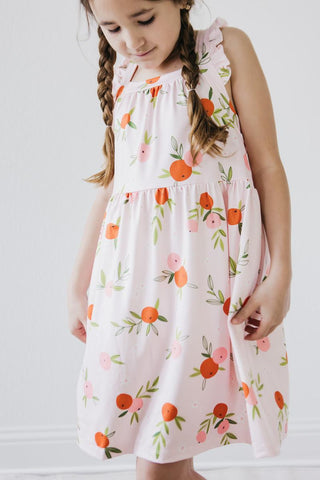 Young girl wearing a pink dress with floral and fruit pattern on a white background