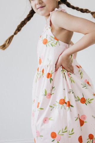 Child wearing a floral dress with an orange and pink pattern on a plain background