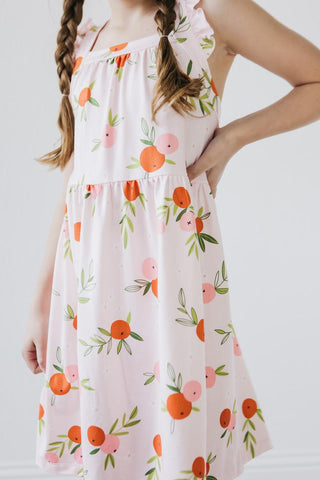 White dress with orange and pink floral pattern worn by a young girl on a white background
