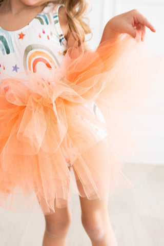 Child wearing a colorful leotard with a rainbow design and an orange tulle skirt.