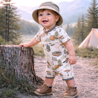 Child in nature-themed outfit standing next to a tree stump with mountains and a tent in the background