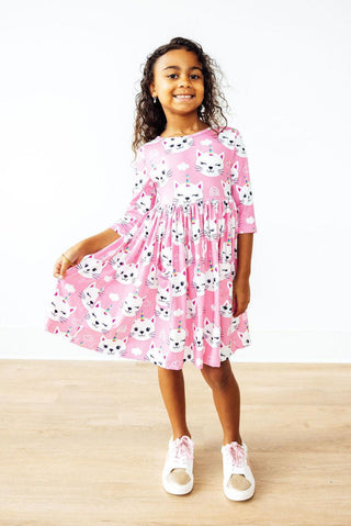Young girl wearing a pink dress with black cat pattern on a white background