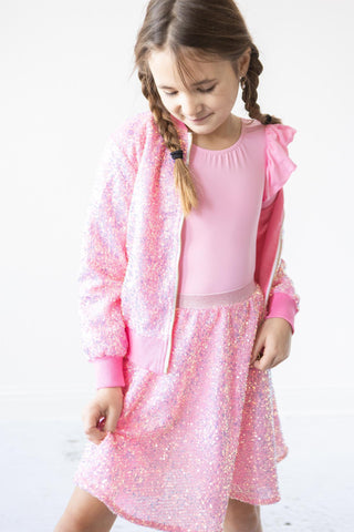 Young girl wearing a pink outfit with a sequin jacket and skirt on a white background