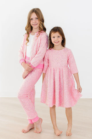 Two children wearing pink outfits and a dress on a white background