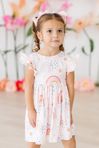 Young girl wearing a white dress with colorful patterns against a blurred floral background