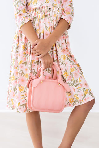 Person wearing a floral dress holding a pink handbag on a white background