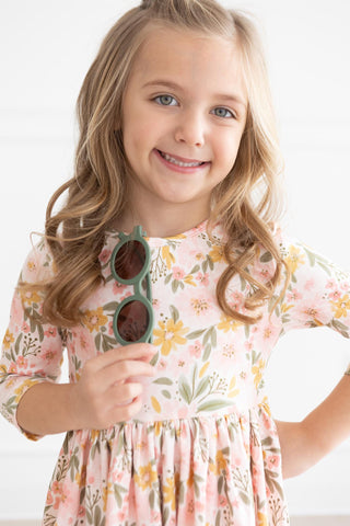 Young girl in a floral dress holding sunglasses against a white background
