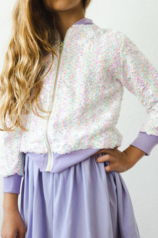 Child wearing a sequined jacket and purple skirt against a white background