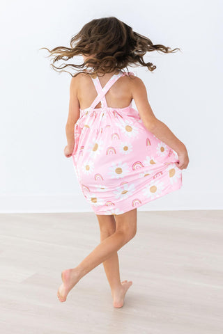 Child wearing a pink dress with rainbow patterns on a white background
