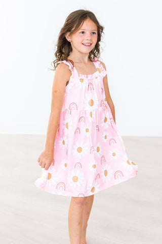 Young girl wearing a pink dress with rainbow patterns on a white background