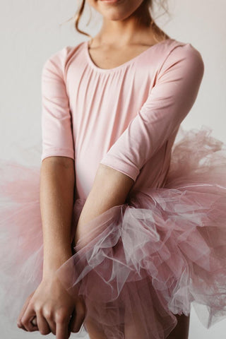 Person wearing a pink ballet outfit with a tutu sitting on a white background