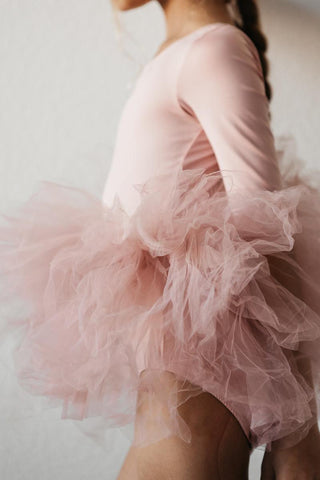 Person wearing a pink tutu leotard with long sleeves against a neutral background