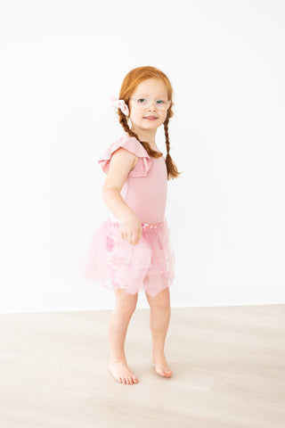 Young girl in a pink dance outfit standing on a white background