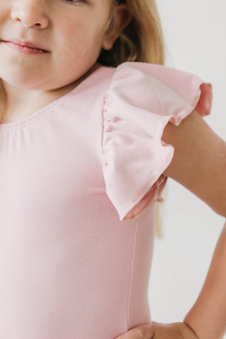 Close-up of a child wearing a pink leotard with ruffled sleeves against a white background