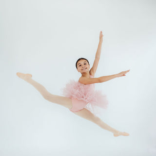 Ballerina in a pink tutu performing a split leap on a white background
