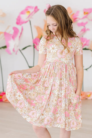 Girl wearing a floral dress with a soft pink and white pattern against a floral backdrop.