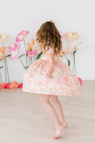 Child in a floral dress standing in front of flowers with a neutral background